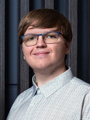 Porträt von Victor Cozea mit Brille und gemustertem Hemd, vor einem dunklen Hintergrund.